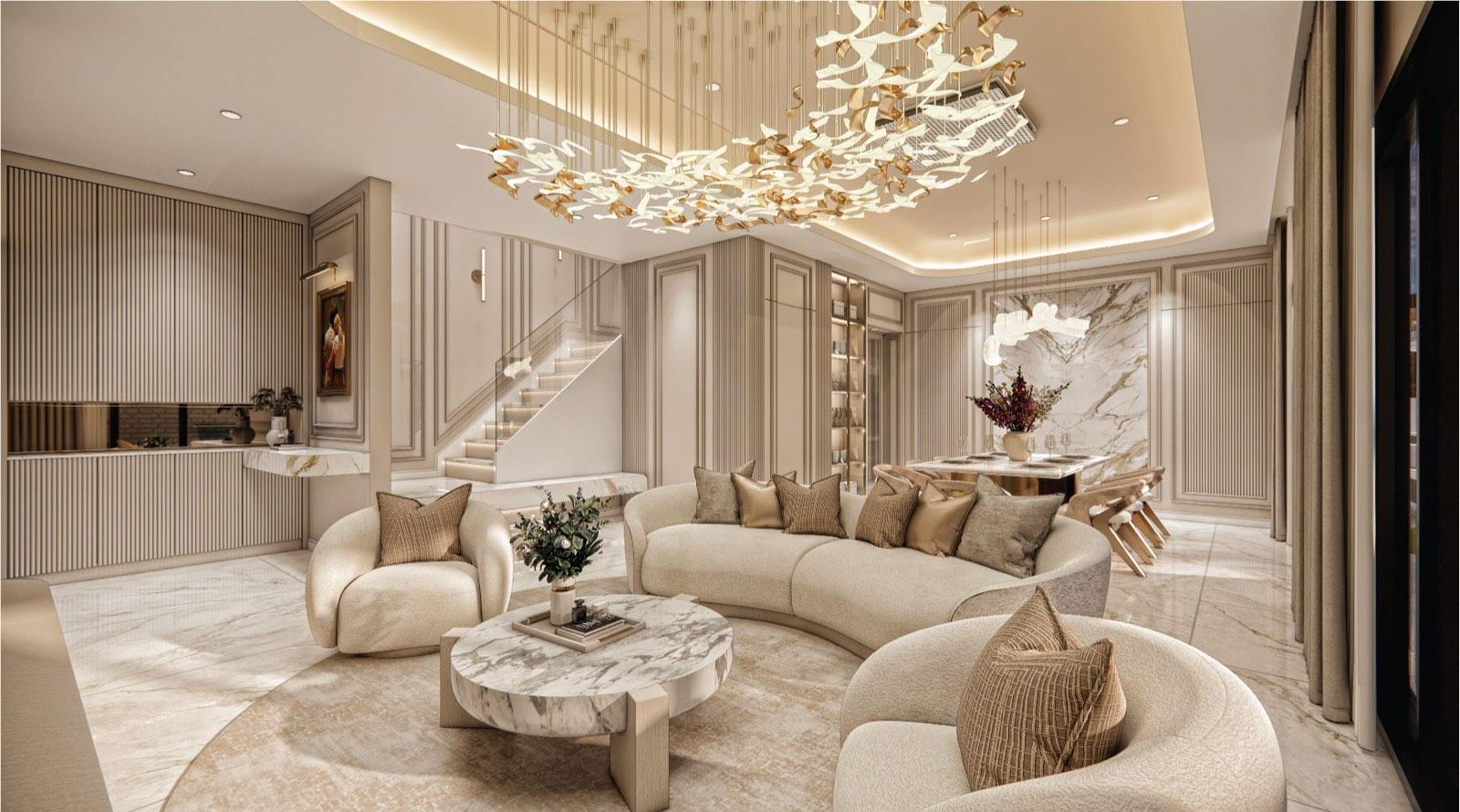 Open living and dining hall at Monarc, Gamuda Gardens beneath a sculptural gold chandelier, with the glass-balustrade stair and calacatta feature wall beyond