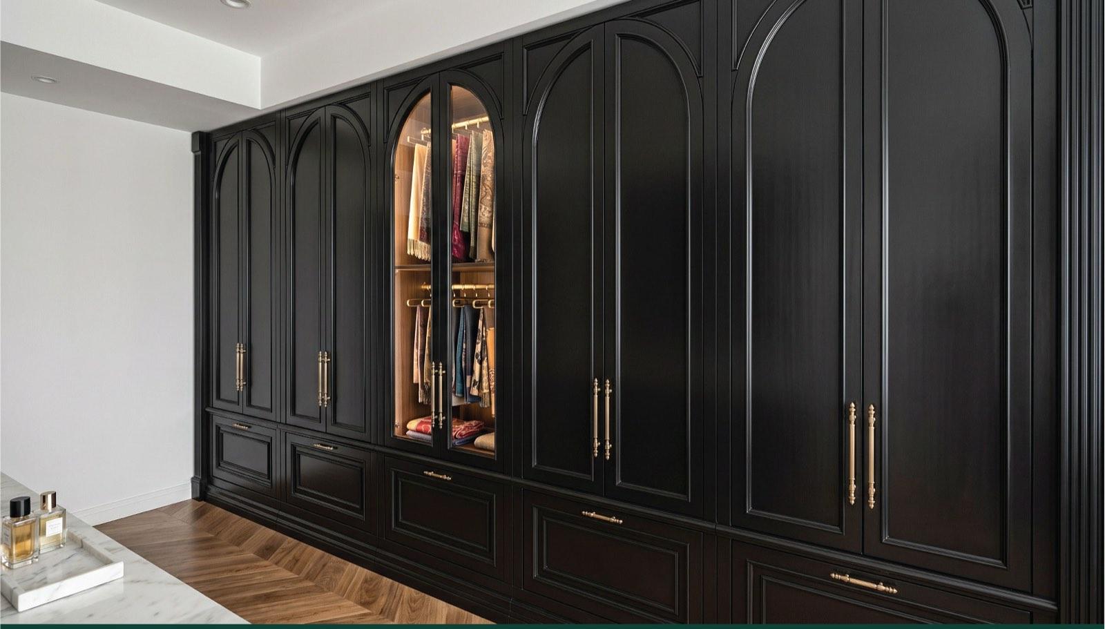 Black arched wardrobe wall with brass pulls and a lit display bay in the Taman Paroi Jaya house