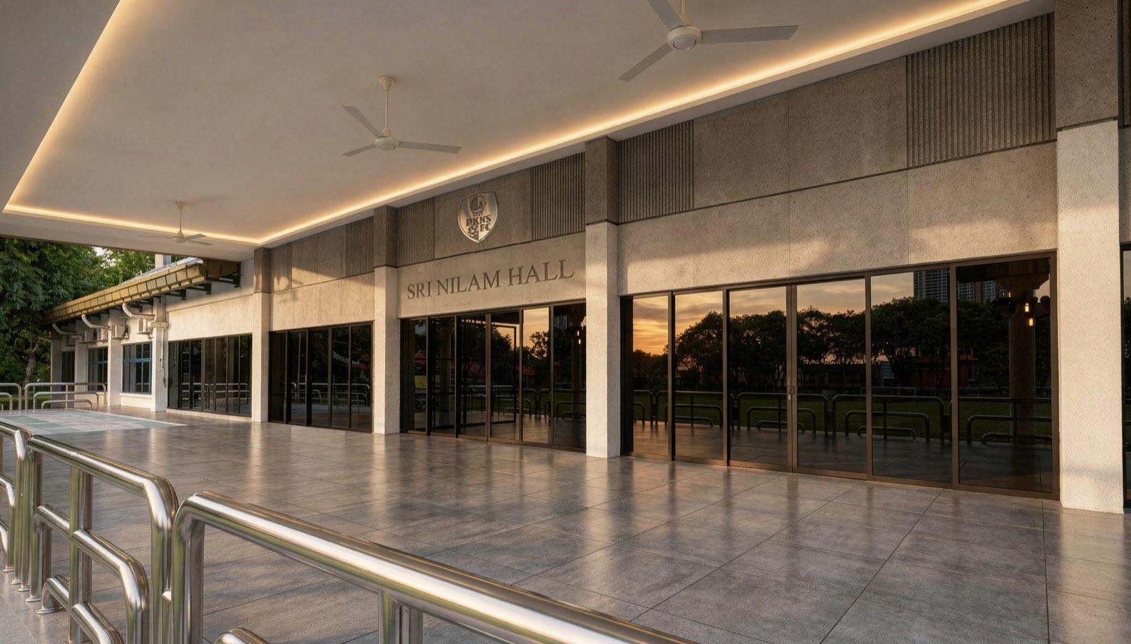 Sri Nilam Hall frontage at dusk in board-marked concrete with full-height glazing and cove lighting